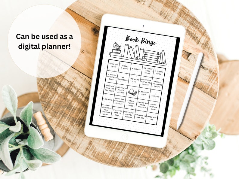 May include: A digital planner on a tablet with a wooden background. The planner displays a "Book Bingo" game with various reading challenges. A white stylus rests beside the tablet. Text in the image reads "Can be used as a digital planner!"