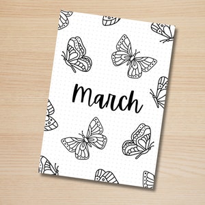 May include: A white notebook cover featuring a pattern of black butterfly illustrations and the word "March" in a handwritten font. The background is dotted.