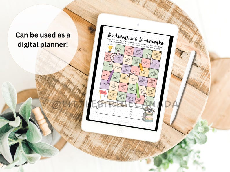 Op de afbeelding: Een witte tablet met een kleurrijk bordspel genaamd Bookworms & Bookmarks met genummerde vakjes, tekstprompts en een styluspen. Het scherm toont een rasterindeling met pastelkleurige vakjes, een startvlag en een lijst voor voortgang.