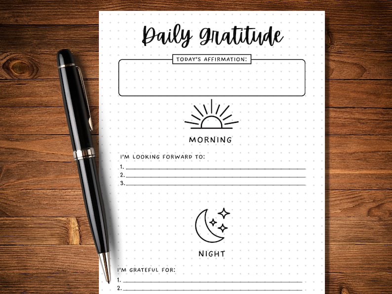 May include: A black and white printable daily gratitude journal with a dotted background. The journal has sections for morning and night. The morning section has a sun icon and the text "I'm looking forward to:" with three lines for writing. The night section has a moon icon and the text "I'm grateful for:" with two lines for writing.
