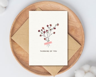 May include: A white card with a simple line drawing of a bouquet of pink flowers tied with a red and white checkered ribbon. The text "Thinking of You" is printed below the flowers.