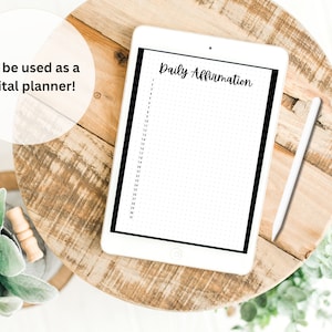 May include: A white digital tablet with a black border displaying a daily affirmation planner. The planner has a dotted grid and the text "Daily Affirmation" at the top. A white stylus is lying on a wooden table next to the tablet.