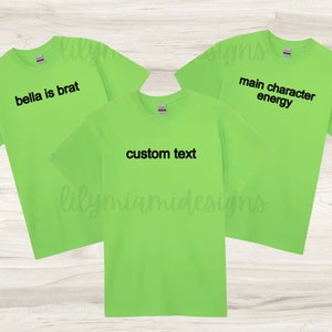 May include: Three neon green t-shirts with black text. One shirt reads "bella is brat", another says "main character energy", and the third says "custom text". The shirts are short-sleeved.