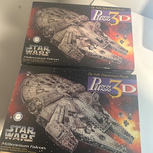 Puede incluir: Dos rompecabezas 3D de Star Wars Millennium Falcon. Cada caja muestra la icónica nave espacial sobre un fondo estrellado. Las cajas dicen "Puzz 3D" y "Millennium Falcon".
