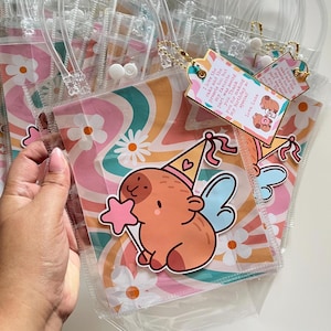 May include: Clear plastic party favor bags with a colorful retro floral design. Each bag features a sticker of a cartoon animal with a party hat and wings. Gold tags with text are attached to the bags.