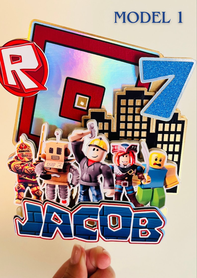 May include: A Roblox themed cake topper with a red and white "R" logo, a blue number 7, and a cityscape. There are five Roblox characters, including a knight, a robot, a builder, a pirate, and a yellow character. The name "JACOB" is written in blue letters on a brick background.