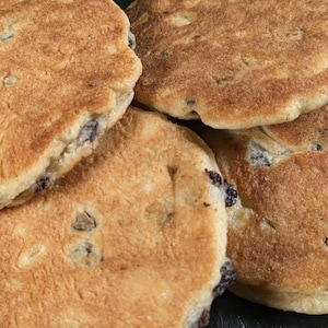 May include: Close-up of four golden brown, round, flat, baked goods with a slightly crispy texture. The baked goods have a few dark brown spots and are stacked on top of each other.