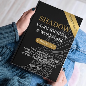 May include: A black book with a gold title that reads "SHADOW WORK JOURNAL & WORKBOOK 2 Books in 1". The book features a gray and white illustration of wings. The text below the title reads "The Comprehensive Subconscious Work Guide to Uncover & Integrate the Shadow Self & Become Whole" and "RENATA MAZU".