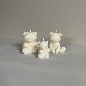Könnte beinhalten: Drei weiße Kerzen in Bärenform in verschiedenen Größen. Die Kerzen stehen auf einer hellgrauen Oberfläche.