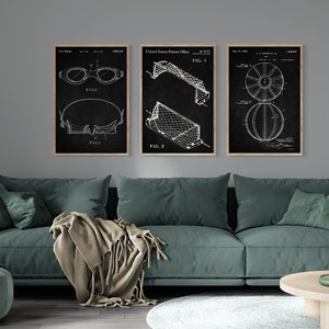 May include: Three black and white patent drawings framed in wood. The drawings depict a pair of swimming goggles, a football goal, and a basketball. The drawings are hung on a grey wall above a green sofa.