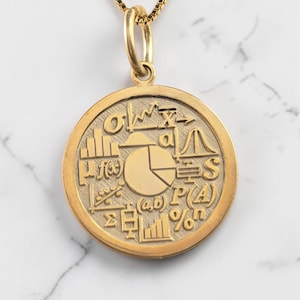May include: A gold-colored pendant necklace featuring a circular charm with mathematical symbols and diagrams. The charm is suspended from a delicate gold chain. The pendant has a matte finish and is set against a marble background.
