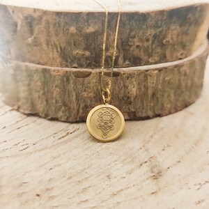 May include: A gold-toned circular pendant necklace featuring a detailed geometric Tree of Life engraving on its face. The pendant is suspended from a delicate gold-toned box chain, showcasing a polished metallic finish and a centred, intricate design.