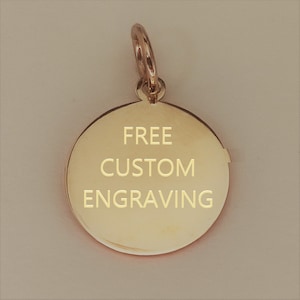 May include: A circular gold-toned metal pendant featuring a polished, reflective surface. The centre of the pendant is engraved with the text "FREE CUSTOM ENGRAVING" in a clean, sans-serif font. A small circular jump ring is attached to the top.