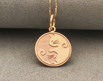 Peut inclure: Un collier avec un pendentif rond en or représentant une silhouette détaillée d'un chat enroulé en cercle. Le pendentif est sur une délicate chaîne en or.