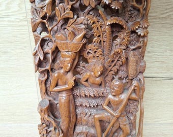 May include: A detailed, brown wooden carving depicting a tropical scene with figures and foliage. The carving shows a woman carrying a basket, a person in water, and a man with a tool, all surrounded by carved trees and plants.
