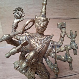 Può includere: Statua in bronzo dettagliata di una divinità con più braccia, probabilmente del sud-est asiatico. La figura è adornata con dettagli intricati, che tiene vari oggetti nelle sue molte mani. La statua ha un aspetto invecchiato, che suggerisce età e utilizzo.