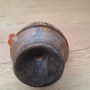 May include: The bottom of a brown clay pot with a hole in the center. The pot has a decorative design around the top edge.