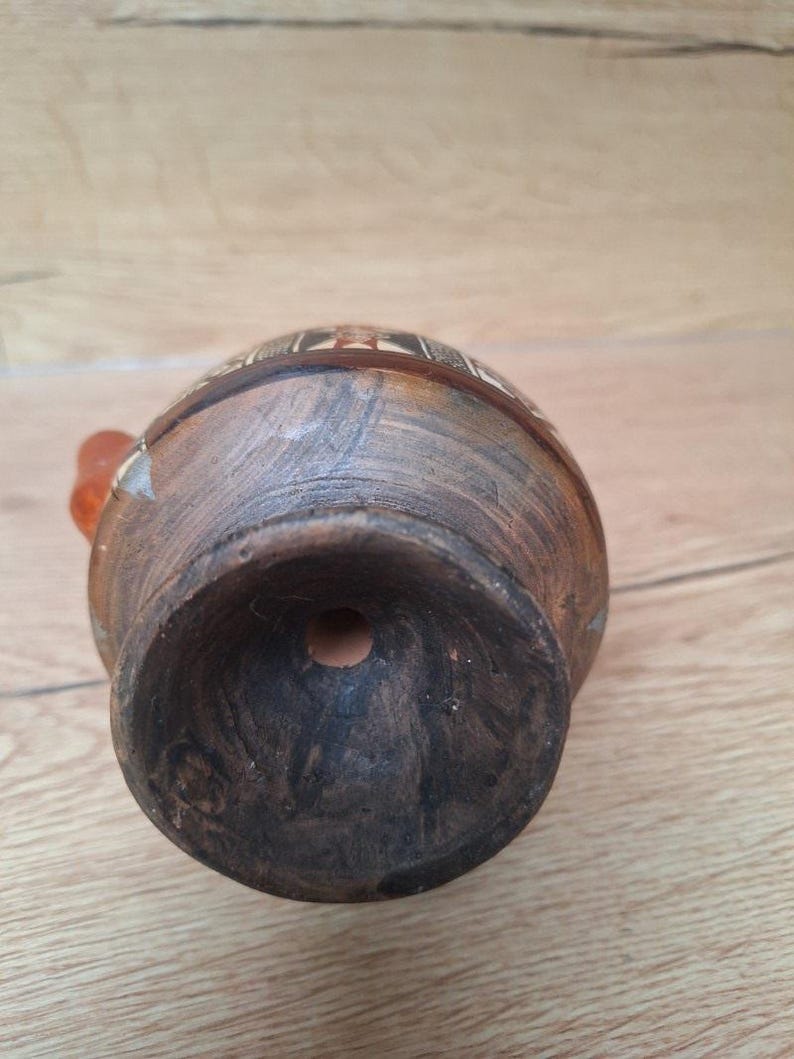 May include: The bottom of a brown clay pot with a hole in the center. The pot has a decorative design around the top edge.