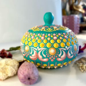 Puede incluir: Caja de cerámica turquesa con tapa, decorada con puntos y remolinos amarillos, rosas y blancos. La caja está pintada a mano con un diseño tipo mandala.