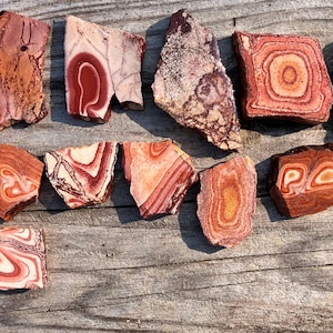 K&ouml;nnte beinhalten: Eine Sammlung von 14 rot, wei&szlig; und braun geb&auml;nderten Achat-Steinen. Die Steine sind in verschiedenen Formen und Gr&ouml;&szlig;en und haben eine nat&uuml;rliche, polierte Oberfl&auml;che.