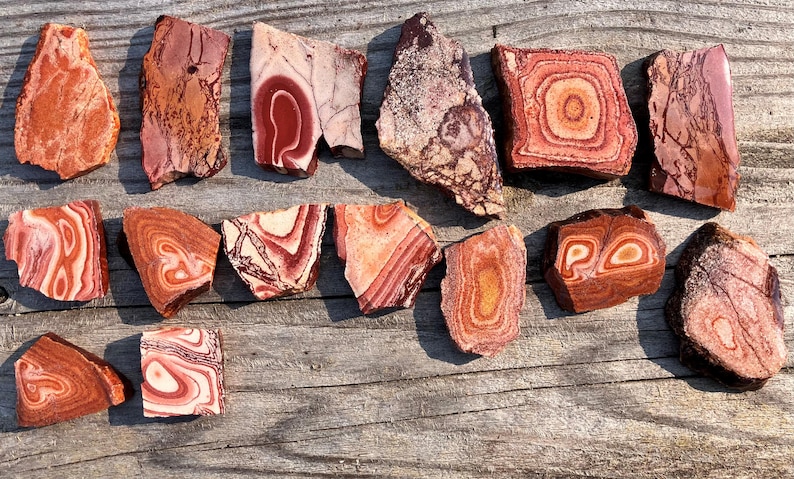 K&ouml;nnte beinhalten: Eine Sammlung von 14 rot, wei&szlig; und braun geb&auml;nderten Achat-Steinen. Die Steine sind in verschiedenen Formen und Gr&ouml;&szlig;en und haben eine nat&uuml;rliche, polierte Oberfl&auml;che.