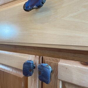 May include: Close-up of three blue agate drawer pulls on wooden cabinets. The pulls are irregularly shaped and have a natural, polished finish.