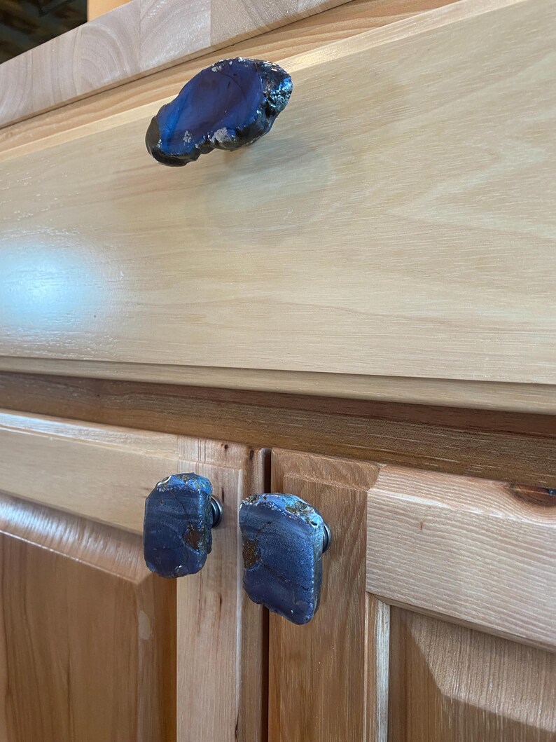 May include: Close-up of three blue agate drawer pulls on wooden cabinets. The pulls are irregularly shaped and have a natural, polished finish.
