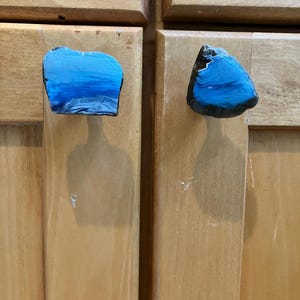 May include: Two blue and black resin cabinet knobs with a unique, abstract design. The knobs are shaped like irregular, flat rocks.