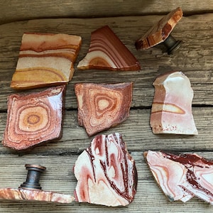 K&ouml;nnte beinhalten: Ein Satz von acht nat&uuml;rlichen Steint&uuml;rgriffen mit verschiedenen roten, orangefarbenen und wei&szlig;en Mustern. Die Griffe sind aus poliertem Stein gefertigt und haben ein einzigartiges, organisches Aussehen.