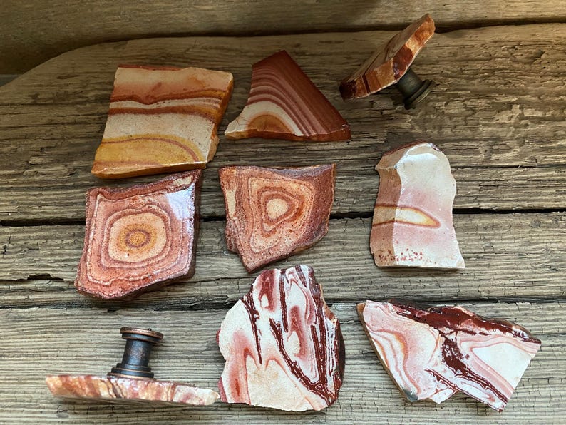 K&ouml;nnte beinhalten: Ein Satz von acht nat&uuml;rlichen Steint&uuml;rgriffen mit verschiedenen roten, orangefarbenen und wei&szlig;en Mustern. Die Griffe sind aus poliertem Stein gefertigt und haben ein einzigartiges, organisches Aussehen.