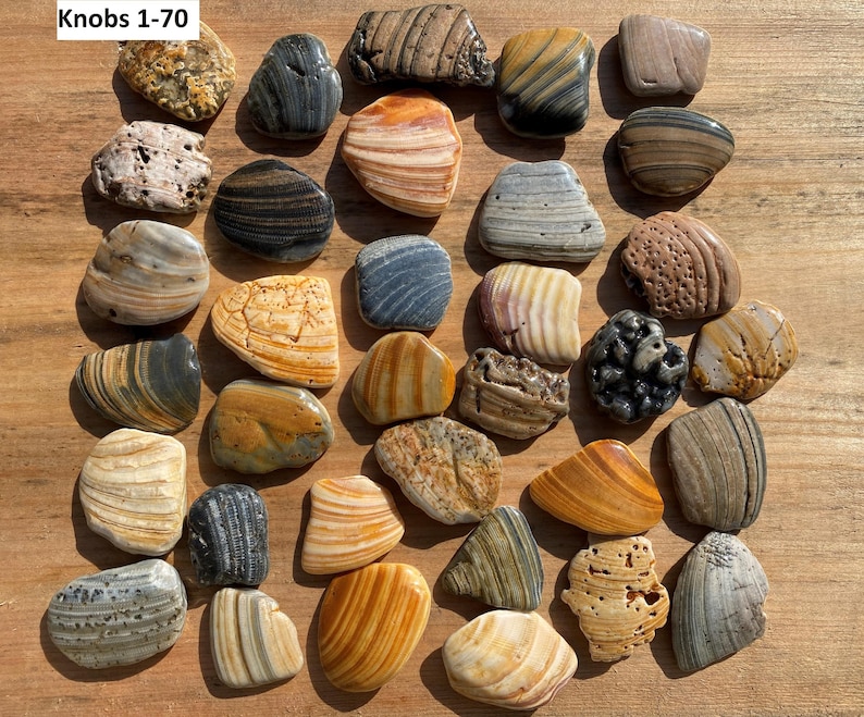 K&ouml;nnte beinhalten: Eine Sammlung von &uuml;ber 30 dekorativen Stein-Kn&ouml;pfen in verschiedenen Formen, Gr&ouml;&szlig;en und Farben. Die Kn&ouml;pfe bestehen aus Naturstein mit gestreiften, gesprenkelten und strukturierten Mustern. Der Text "Knobs 1-70" befindet sich in der oberen linken Ecke.