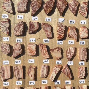 K&ouml;nnte beinhalten: Eine Sammlung von 36 einzigartigen, bunten und gemusterten Steinplatten, nummeriert von 361 bis 395. Die Platten sind in Reihen auf einer Holzoberfl&auml;che angeordnet.