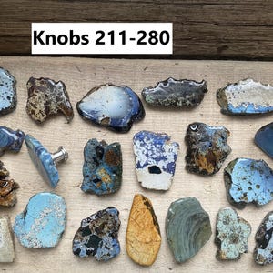May include: A collection of 17 ceramic knobs in various shades of blue, brown, and white. The knobs are irregularly shaped and have a rustic, handmade appearance. The text "Knobs 211-280" is visible at the top of the image.