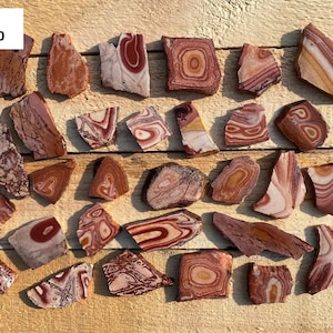 May include: A collection of 25 red, white, and brown banded agate slices. The agate slices are various shapes and sizes. The agate slices are arranged on a wooden surface. Knobs 361-430.