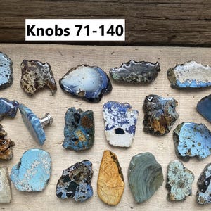 May include: A collection of 18 unique ceramic knobs in various shades of blue, brown, and white. The knobs are irregularly shaped and have a rustic, handmade appearance. The text "Knobs 71-140" is visible at the top of the image.