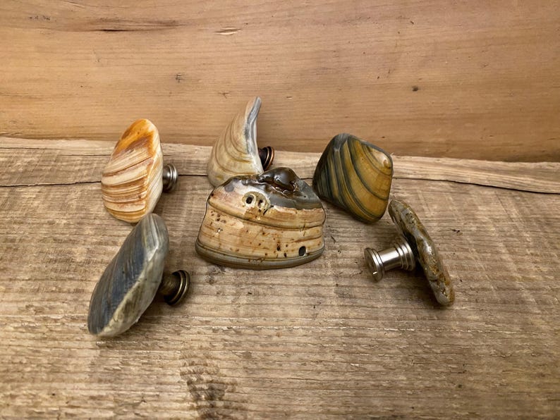 以下が含まれることがあります： 天然石で作られた、ユニークで手作りのキャビネットノブ6個。各ノブは、ブラウン、ベージュ、グレー、イエローなど、異なるパターンと色の組み合わせが特徴です。ノブは金属製のベースに取り付けられています。