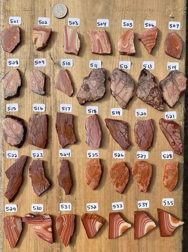 K&ouml;nnte beinhalten: Eine Sammlung von 35 Natursteinplatten, jede mit einzigartigen Mustern und Farben, die von Hellrosa bis Dunkelrot reichen. Die Platten sind in Reihen auf einer Holzoberfl&auml;che angeordnet und mit Nummern von 501 bis 535 beschriftet.