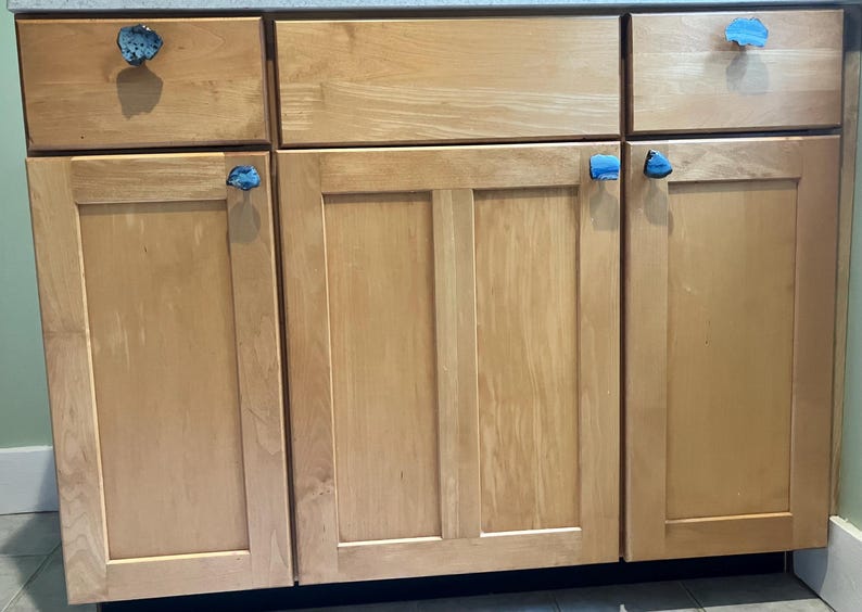 May include: A set of five wooden cabinet doors with blue agate stone knobs. The cabinet doors are a light wood color and have a smooth finish.