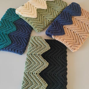 Può includere: Cinque pochette all'uncinetto fatte a mano in vari colori: verde acqua, blu navy, verde oliva, beige e nero. Ogni pochette presenta un motivo a zig-zag sul bordo superiore e un design a punto strutturato.