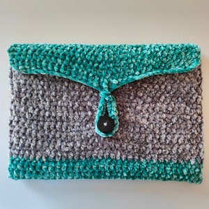 Op de afbeelding: Een grijze en turquoise gebreide clutch met een zwarte knoopsluiting.