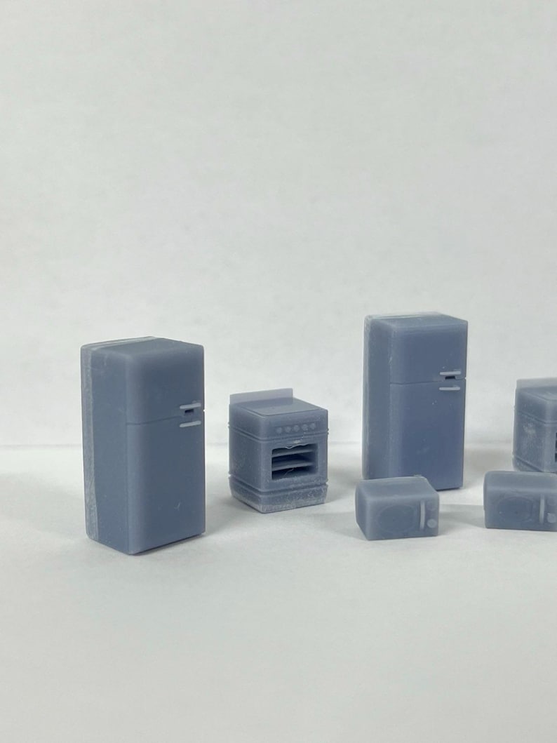 Puede incluir: Un conjunto de electrodom&eacute;sticos de cocina en miniatura, que incluye un refrigerador, un horno y dos electrodom&eacute;sticos m&aacute;s peque&ntilde;os, todos de color gris claro.