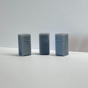 Op de afbeelding: Drie miniatuur grijze koelkasten zijn in een rij gerangschikt. Elk heeft een rechthoekige vorm met een deur en een handvat. De objecten staan tegen een effen witte achtergrond.
