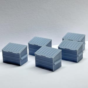 May include: Five grey plastic miniature dumpsters, each with a lid and a textured surface. The dumpsters are arranged in a staggered pattern on a white surface.