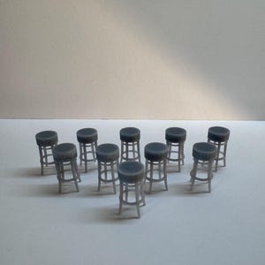 May include: A collection of miniature grey bar stools. Each stool has a round, dark grey seat and a light grey, four-legged base. The stools are arranged in a group on a white surface.