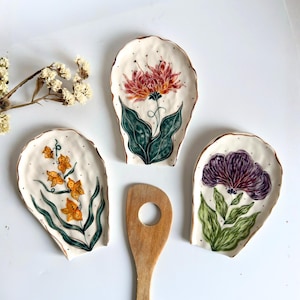 May include: A set of three ceramic mugs with a speckled, matte finish. The mugs are in shades of cream, light gray, and dark gray. Each mug has a simple, minimalist design and a rounded handle.