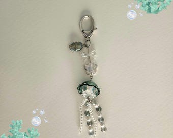 May include: A silver key chain with a green and white jellyfish charm, a silver fish charm, and a silver flower charm. The jellyfish charm has white beads hanging from it.