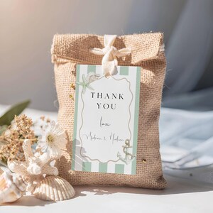 May include: A burlap gift bag with a tag that reads "THANK YOU" in black script. The tag has a light green and white striped background with a starfish and anchor illustration. The bag is tied with a white ribbon and is decorated with seashells.
