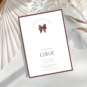 Könnte beinhalten: Eine weiße Einladung mit einem weinroten Rand und Text. Die Einladung lautet "Feiern Sie mit uns eine Brautparty" und "Zu Ehren von Chloe". Oben befindet sich eine weinrote Schleifengrafik. Datum, Uhrzeit und Ort sind ebenfalls angegeben.