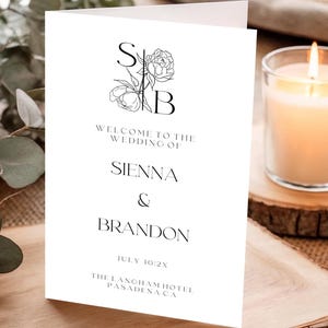 May include: A white wedding program with black text. The program reads "Welcome to the Wedding of Sienna & Brandon" with the date and venue. A floral design with the letters "S" and "B" is at the top.
