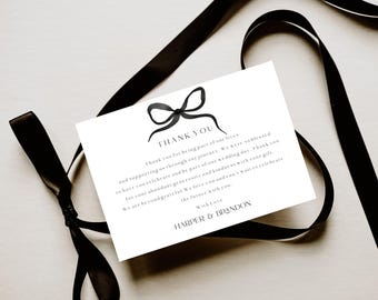May include: A white card with a black bow illustration and the words "THANK YOU" in black. The card is surrounded by a black ribbon. The text on the card reads "Thank you for being part of our lives..." and is signed "HARPER & BRANDON."